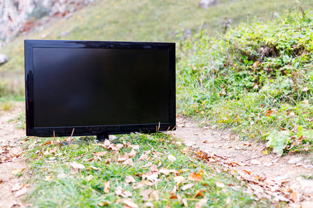 old black flat screen tv on the field road, autumn leaves on the road and tvの写真素材