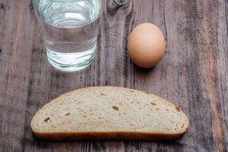 glass of water an egg and a slice of black bread on a wooden table, poor lunch, financial problemsの写真素材
