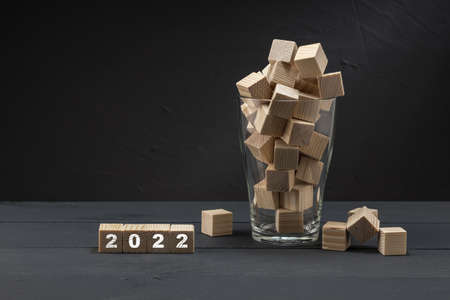 a hollow glass glass is filled with wooden cubes of which a lot they spill over the edge, next to the cube is written 2022の写真素材