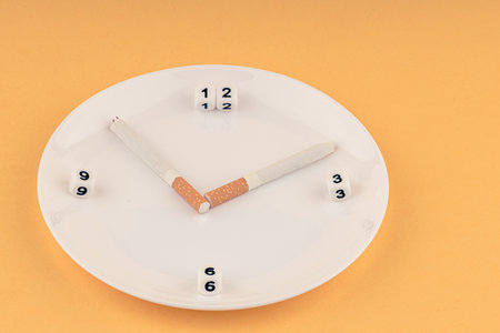 a clock made of cigarettes and a dial, a plate and cigarettes on it represent a clock. ten minutes past tenの写真素材