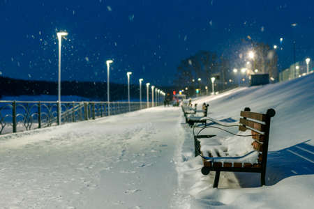 a row of empty park benches in the wintertime it is snowing. blurred snowflakes fly in the air,...