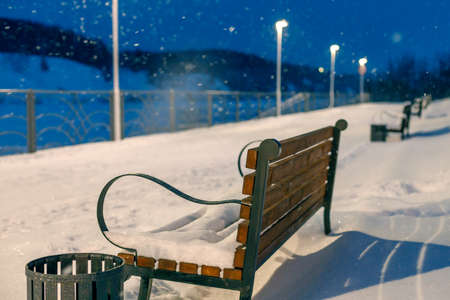empty benches in a winter evening during a snowfall in the park. rear view of bench and lantern lightingの写真素材