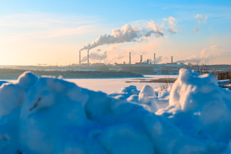 a lot of snow in the foreground, a steaming plant with a lot of chimneys in the background....