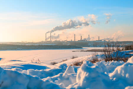 on a cold winter day on the other side of the frozen river a smoking factory, a large amount of work with smokeの写真素材