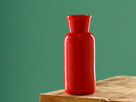 bright red vase on the edge of a wooden table on a green background. empty vaseの写真素材
