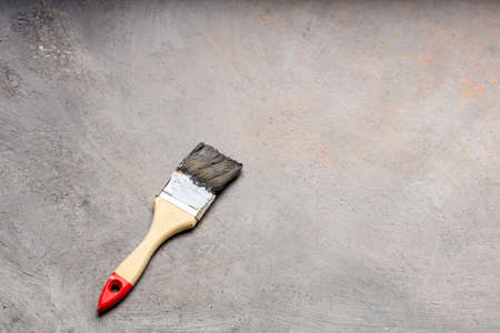 old paint brush on gray canvas covered with unevenly paint. paint brush with wooden handle on gray backgroundの写真素材