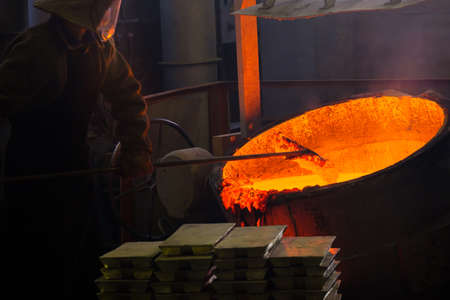 a caster at work at a molten vat with red metal, hard work in hot production. hot metal