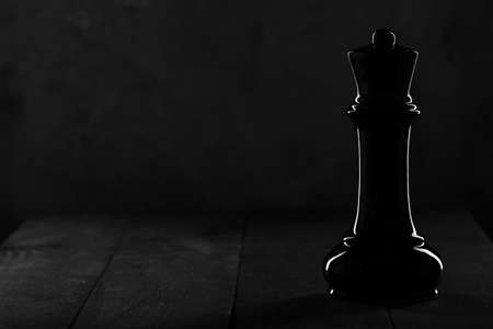 Black chess piece queen standing out on a black background. glare on the figureの写真素材