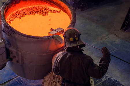 top view of a vat with red molten metal and a worker checks the consistency state before pouring....