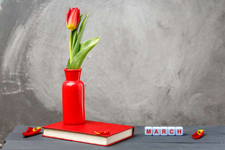red vase with red tulips on a gray background. next to the vase there is an inscription - March....