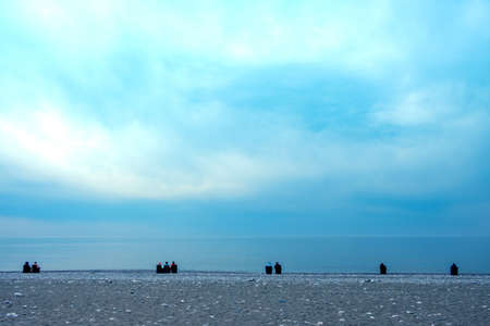 a group of people on chairs sitting by the sea look into the distance, the cloudy sky and the calm...