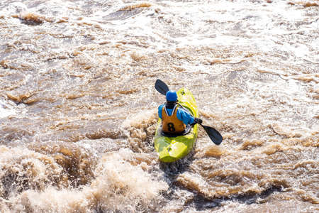 a man in a yellow kayak floats on a mountain river. dangerous rapids on a muddy mountain riverの写真素材