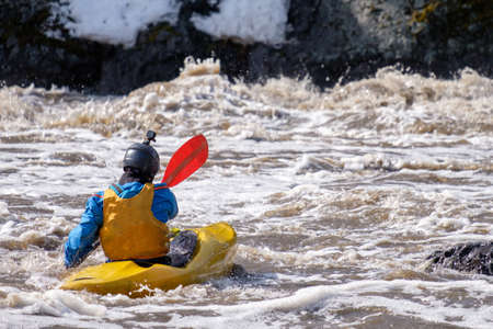 a man in a kayak rowing in the waters of a turbulent mountain river. difficult route. dirty water of the spring riverの写真素材