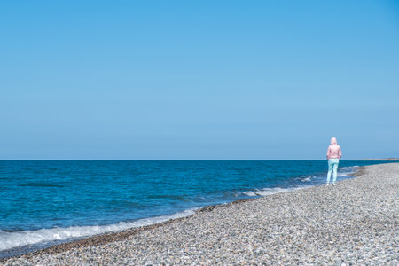 girl in a hood on the seashore, the girl's pants match the color of the sky. walk by the seaの写真素材