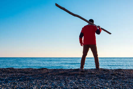 a man in a red jacket on the seashore with a stick on his shoulder. lonely man by the sea. dangerous man by the seaの写真素材