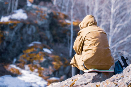 the traveler sitting with his back to us on the rock. thoughtfulness in nature. reflections sitting on a stone in the mountainsの写真素材