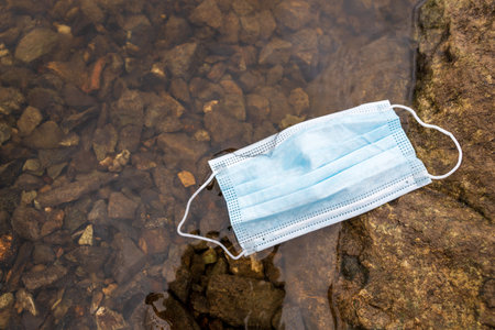 garbage in the water, medical mask on the river bank. pollution of rivers with a new type of wasteの写真素材