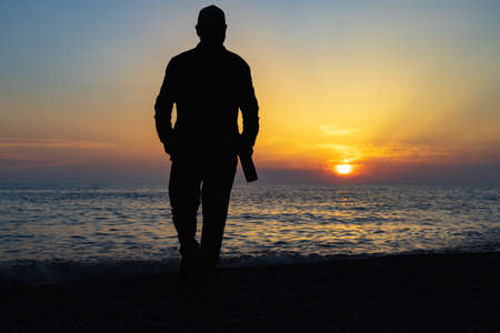 silhouette of a man walking along the sea with a bottle during sunset. wine walks by the seaの写真素材