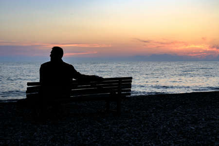 silhouette of a man sitting on the seashore at sunset time. loneliness at sea, rest alone