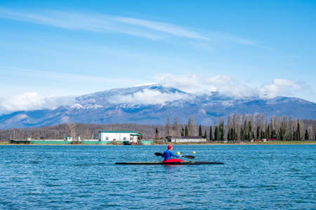 a man rower floats on a kayak rowing oars. background mountain landscape. rest at natureの写真素材