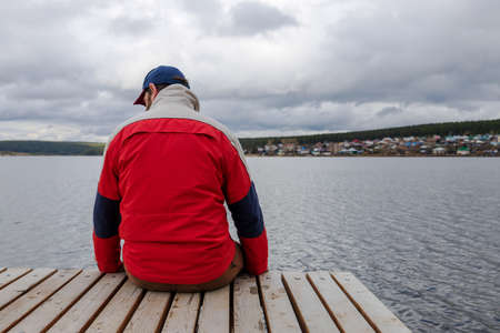 a man against the backdrop of a pond sits on the pier. rest from city life in the countrysideの写真素材