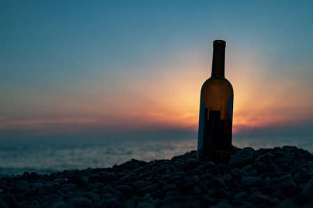 a bottle of wine is stuck in a pebble by the sea. bottle on the background of the sea sunsetの写真素材