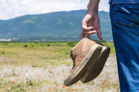 close-up of shoes in male hands on the background of the field. summer day, tired traveler