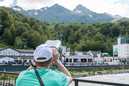 a man in a green T-shirt looks at the mountains through binoculars. Russia Sochi