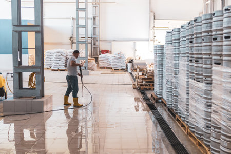 an employee in a production facility in a large room washes the floor with a strong jet of water. water on the floor in the room while washingの写真素材
