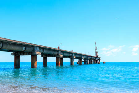 pier on the sea coast in daylight, blue sea and blue sky. old pier and light wavesの写真素材