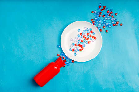 blue and red plastic stars spill out of the vase and land on the plate. blue fabric surfaceの写真素材