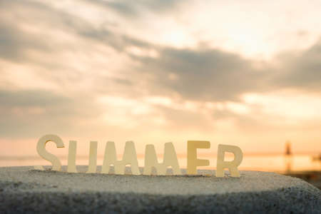 inscription summer from letters inserted into the sand against the background of a summer landscape on a pond. summer evening on the pondの写真素材