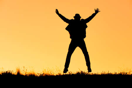 silhouette of a man jumping for joy in a hat, arms and legs in different directions. the background...