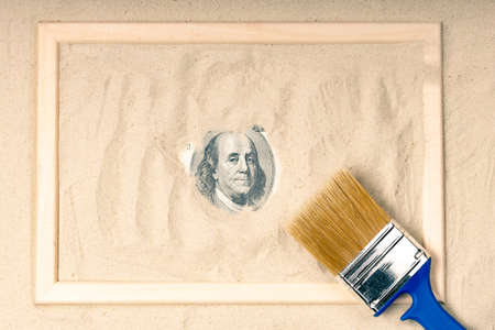 one hundred dollars in a wooden frame on the sand, next to it is a brush to remove sand. historical...