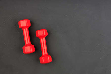 two red dumbbells in the corner of a black background. sports equipment itemsの写真素材