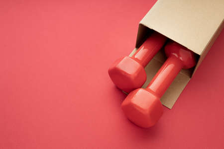 two red dumbbells are visible from a paper box on a red background. package with dumbbellsの写真素材