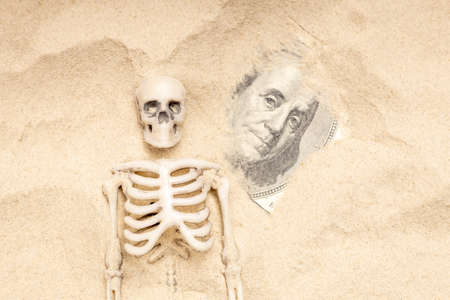 a human skeleton in the sand against the background of a dollar bill. drought and money problemsの写真素材