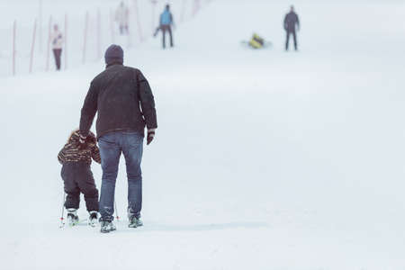 parent holding child skiing, father and son winter day training