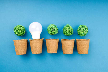 a row of five pots for plants in one of them is a light bulb, in the other four pots are green...