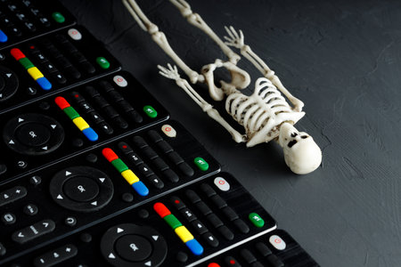 the skeleton of a person lies diagonally down, parallel to it are remote controls from the TV. death and life of a person are accompanied by televisionの写真素材