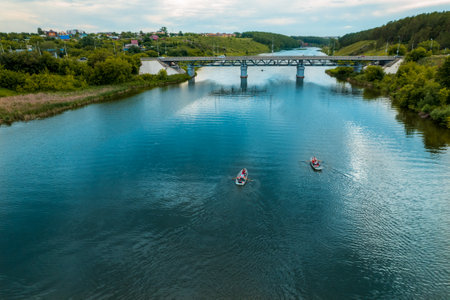 two rowing boats are sailing on the river. bridge over the river on a summer day. nature on the shore and the river view from the droneの写真素材