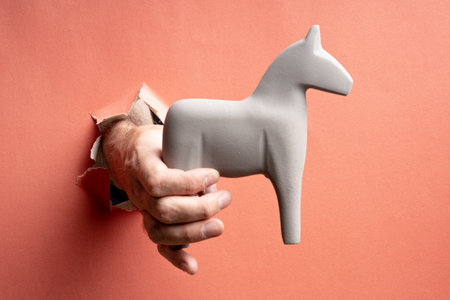 hand pokes through torn paper. the horse is held in hand. gift through the hole. donate a trojan horseの写真素材
