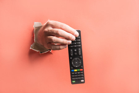 the hand breaks through the paper and demonstrates the remote control for the TV. remote control...