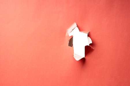a through hole in peach-colored paper with torn edges. uneven torn paper surface. empty space in a holeの写真素材