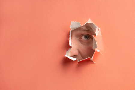 peep through torn paper, look through a hole in paper. a man eye looks through a hole