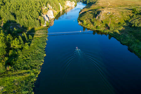 view from above on the bend of the river along which the boat floats, a suspension bridge across the...