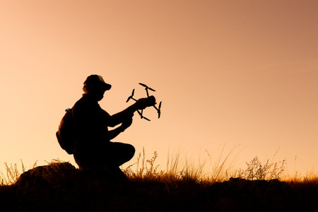 silhouette of a man in a cap squatting with a drone in his hands. outside, the launch of an aircraft...