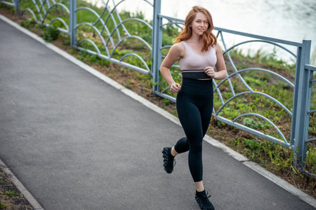 a red-haired sports girl in sportswear running along the embankment. summer evening by the river, doing sportsの写真素材