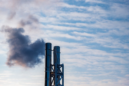 two chimneys on the background of the sky with clouds, the smoke from the chimney is dark. dark smoke from the boiler roomの写真素材