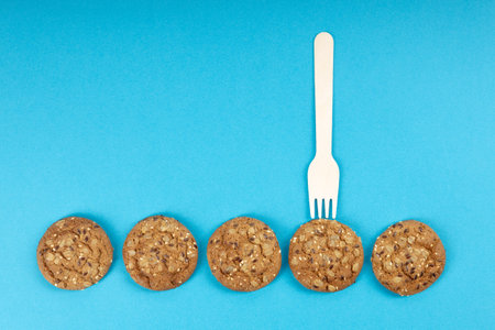 a row of five round oatmeal cookies are laid out in a row, a fork over one cookie. blue background